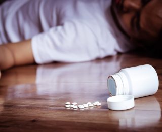 depression man committing suicide by overdosing on medication. close up of overdose pills from plastic medicine container with depress man on the floor